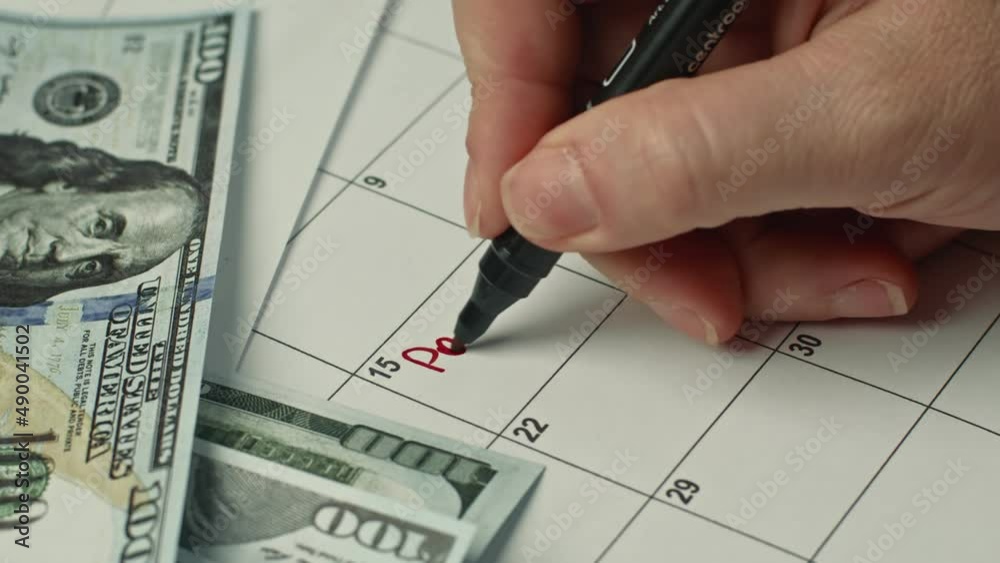Female hand marking the PAY DAY in calendar as a reminder using a red pen. Scheduling and planning concept Female hand marking the PAY DAY in calendar as a reminder using a red pen. Scheduling and planning concept