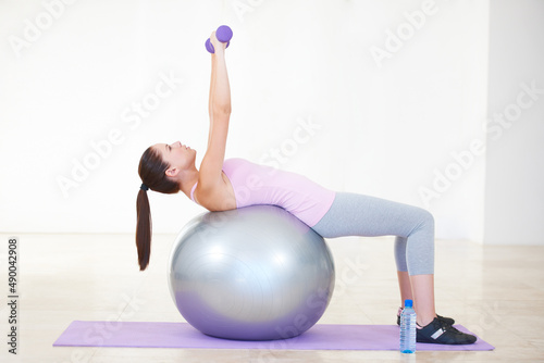 Balance and strength. Full length shot of a young woman lying back on an exercise ball and lifting weights.