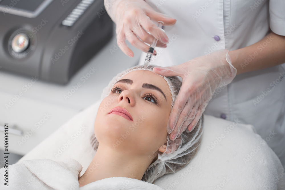 Naklejka premium Woman gets injection in her face. Beauty woman giving botox injections. Young woman gets beauty facial injections in the cosmetology salon. Face aging injection. Aesthetic Medicine, Cosmetology