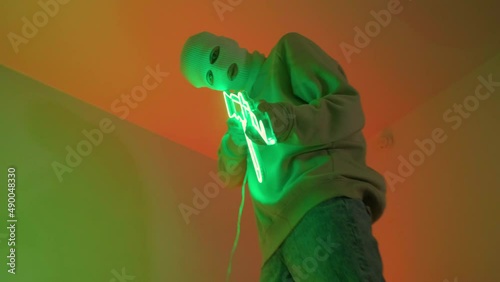 A gangster in a white mask holds a neon machine gun. A young guy exhales smoke from an electronic cigarette into the camera. Video 4k for a rap clip in a neon room.