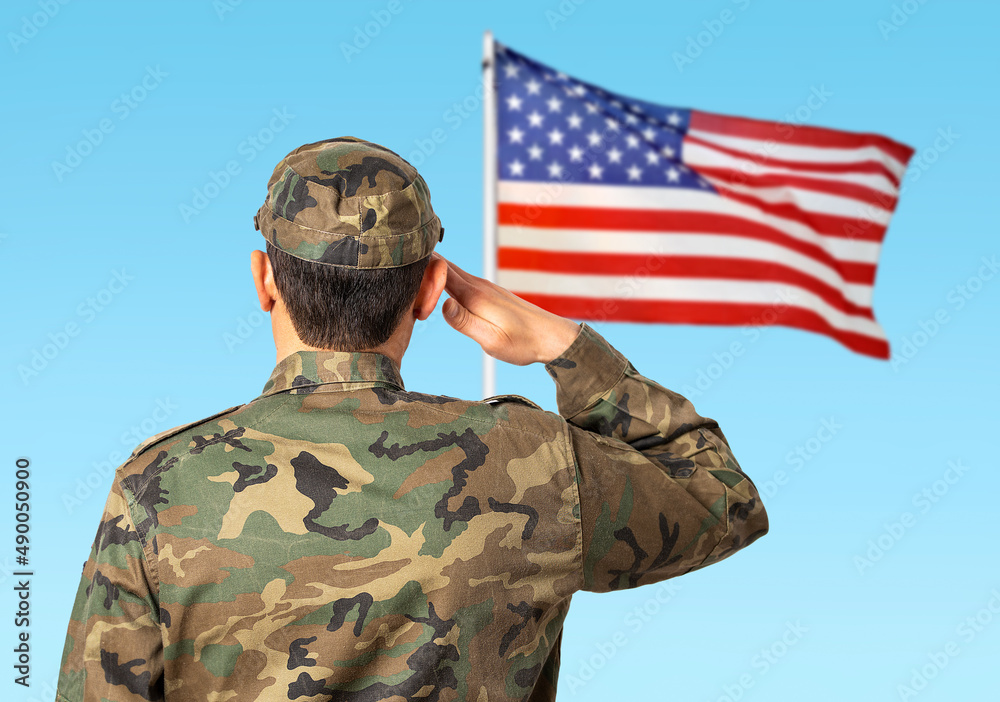 Rear view of a young soldier standing to a the US flag and saluting Rear view of a young soldier standing to a the US flag and saluting
