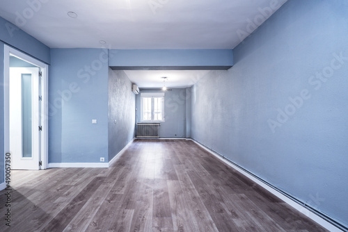 Empty room with cast iron radiator, air conditioner, white wood carpentry, blue painted walls and wooden flooring