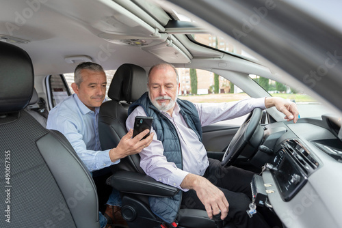 middle-aged passenger in back seat showing his smartphone to older driver - concept of transportation, cab, taxi and technology