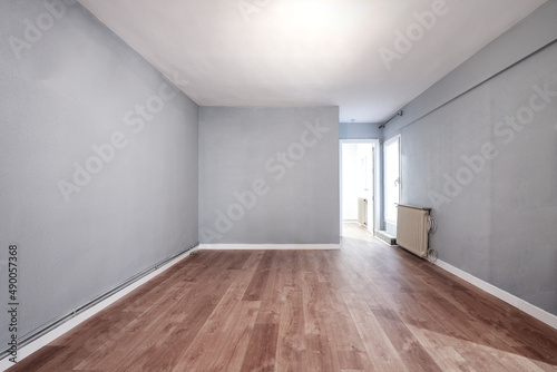 Empty room with cast iron radiator  white woodwork  gray painted walls  exit to a terrace and wooden floor
