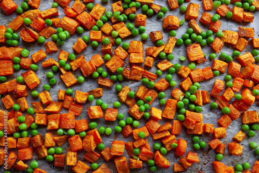 Fototapeta premium Oven roasted carrots and sweet potatoes and green peas on a parchment paper, cut into cubes
