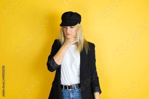 Beautiful woman wearing casual white t-shirt and a cap over isolated yellow background touching painful neck, sore throat for flu, clod and infection photo