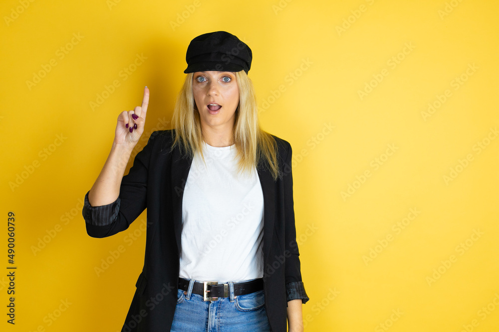 Beautiful woman wearing casual white t-shirt and a cap over isolated yellow background surprised and thinking with her finger on her head that she has an idea. Beautiful woman wearing casual white t-shirt and a cap over isolated yellow background surprised and thinking with her finger on her head that she has an idea.
