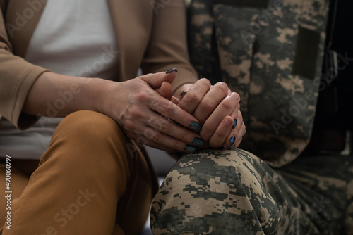 Close up of male and female hands holding each other gently. Man soldier in military uniform taking hand of woman, his girlfriend or wife. Happy meeting concept. photo