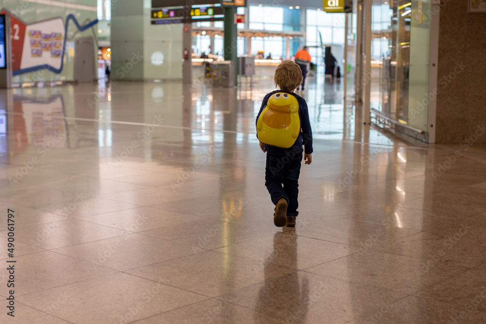 Obraz premium Cute baby boy waiting boarding to flight in airport transit hall near departure gate. Active family lifestyle travel by air with children