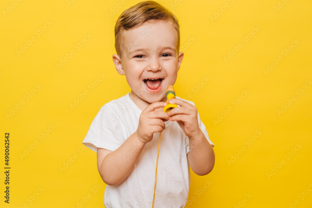 Portrait of a cute laughing little boy on a yellow background with a toy in his hands. Copy space. Portrait of a cute laughing little boy on a yellow background with a toy in his hands. Copy space.