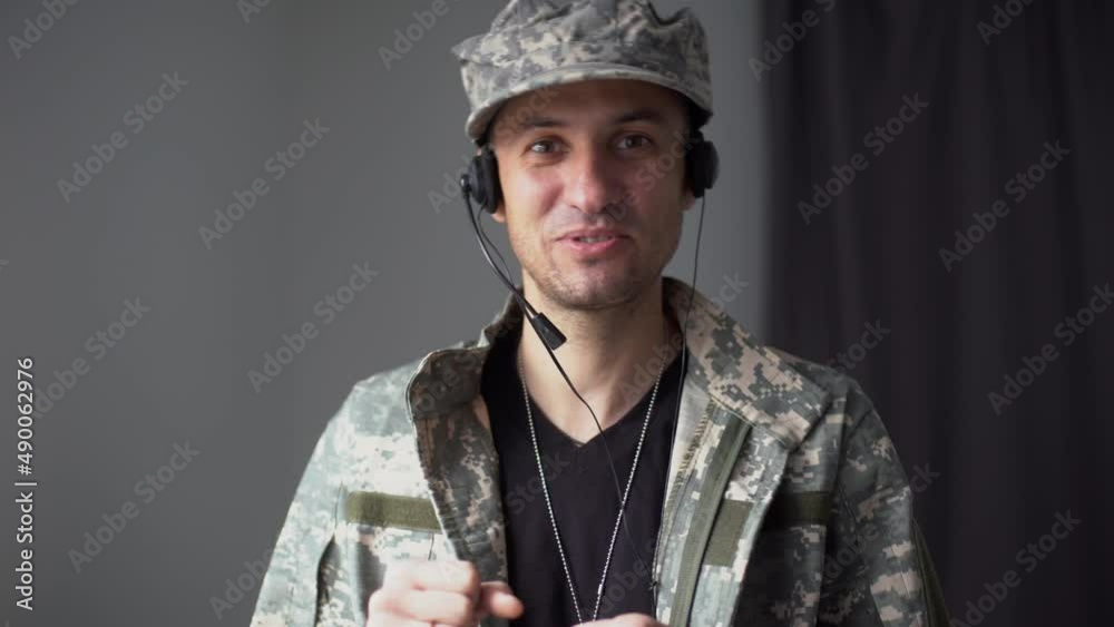 military man in headphones talking in slow motion looking at camera. Video chat POV portrait of brave male soldier conferencing online standing indoors military man in headphones talking in slow motion looking at camera. Video chat POV portrait of brave male soldier conferencing online standing indoors