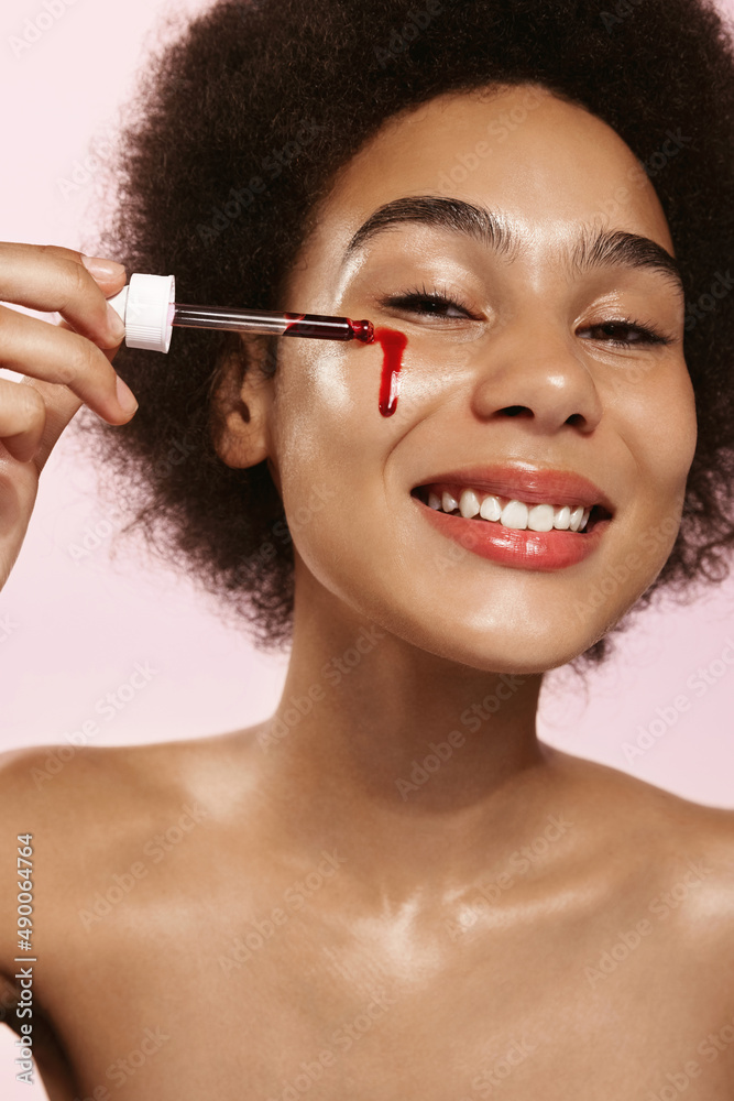 Obraz premium Beauty african woman, naked shoulders and nude face, apply serum vitamin c, argan oil tea tree ingredients in pippette dropper under eye, treating skin for nourishing and moisturizing effect