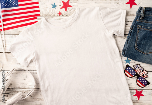 Mockup design white t shirt for logo, top view on white wooden background with US flag, shoes and jeans © dark_blade
