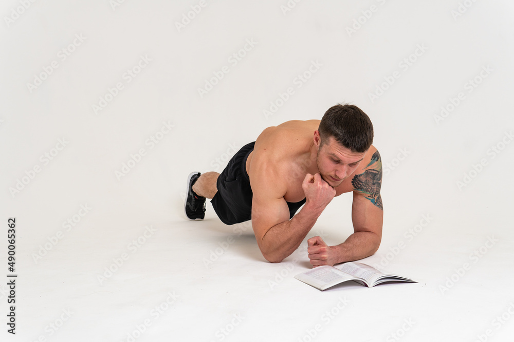 Bodybuilder reads the book on a white background isolated at the bottom of his head on his hands man young muscular, athletic fitness white background muscles, sexy fit. ABS gym, beach tan Bodybuilder reads the book on a white background isolated at the bottom of his head on his hands man young muscular, athletic fitness white background muscles, sexy fit. ABS gym, beach tan