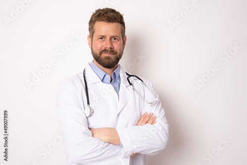Young smiling male doctor posing with arms folded isolated on white background with copy space on the right side © Danko