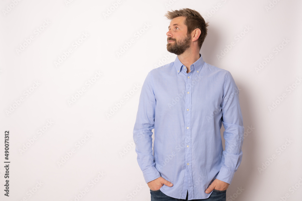 Portrait of charming successful young man in blue shirt, smiling broadly with self-assured expression while holding hands in pockets over white background. Business concept. Portrait of charming successful young man in blue shirt, smiling broadly with self-assured expression while holding hands in pockets over white background. Business concept.