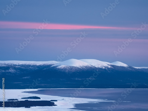Snow-covered polar cone hills in winter early in the morning. Winter polaris landscape. View of the snow-covered hills and White sea. Cold winter weather. Harsh northern climate background.