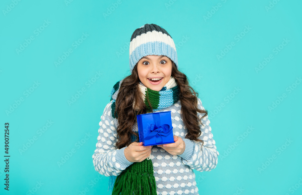 amazed child in knitwear hold box. kid with present. teen girl on blue background. winter holidays