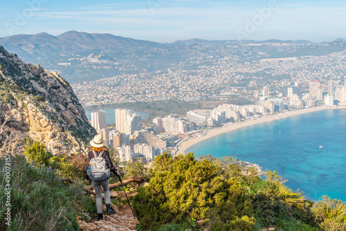 A young hiker descending from the top of the Penon de Ifach Natural Park with the city of Calpe in the background, Valencia. Spain. Mediterranean sea. View of La Fossa beach