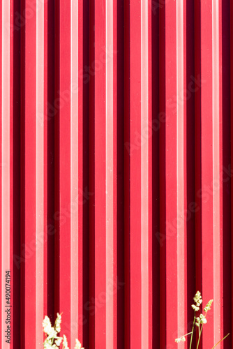 Fragment of a red fence made of corrugated board. Construction and repair. Vertical.