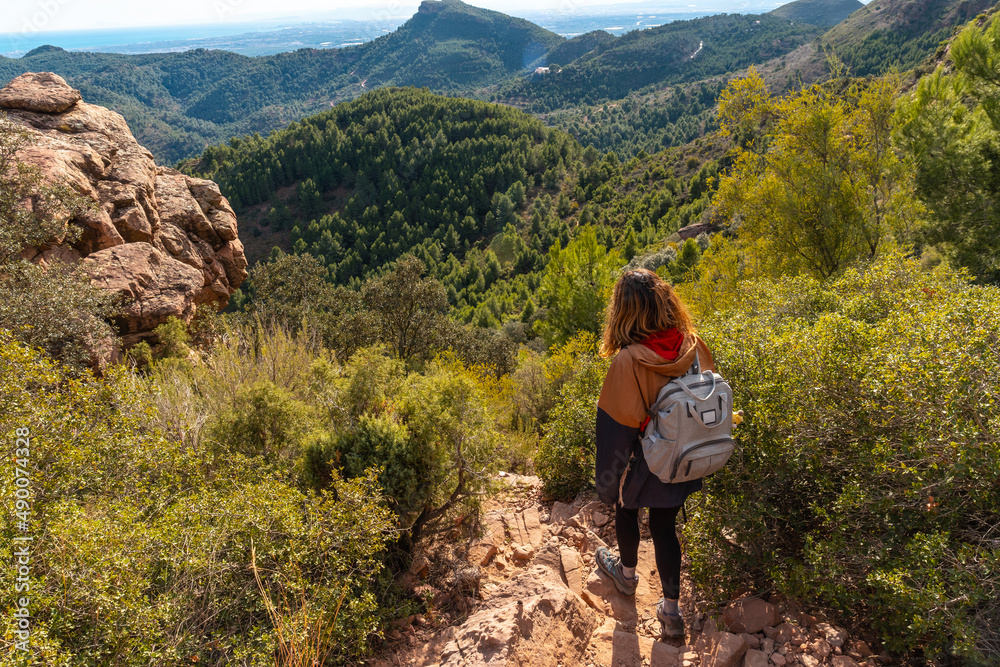 Naklejka premium A young hiker girl descending from the top of the El Garbi mountain, the spectacular viewpoint of the Sierra Calderona, Valencia, a 593-meter mountain. Mediterranean Sea. Spain