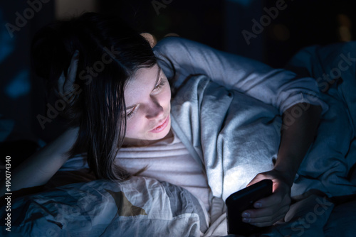 Young girl in a bed with a phone at night.