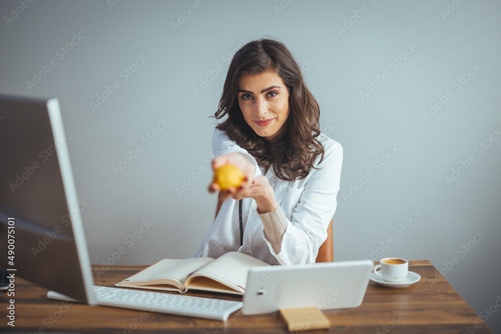 Smiling nutritionist in her office, she is showing healthy vegetables ...