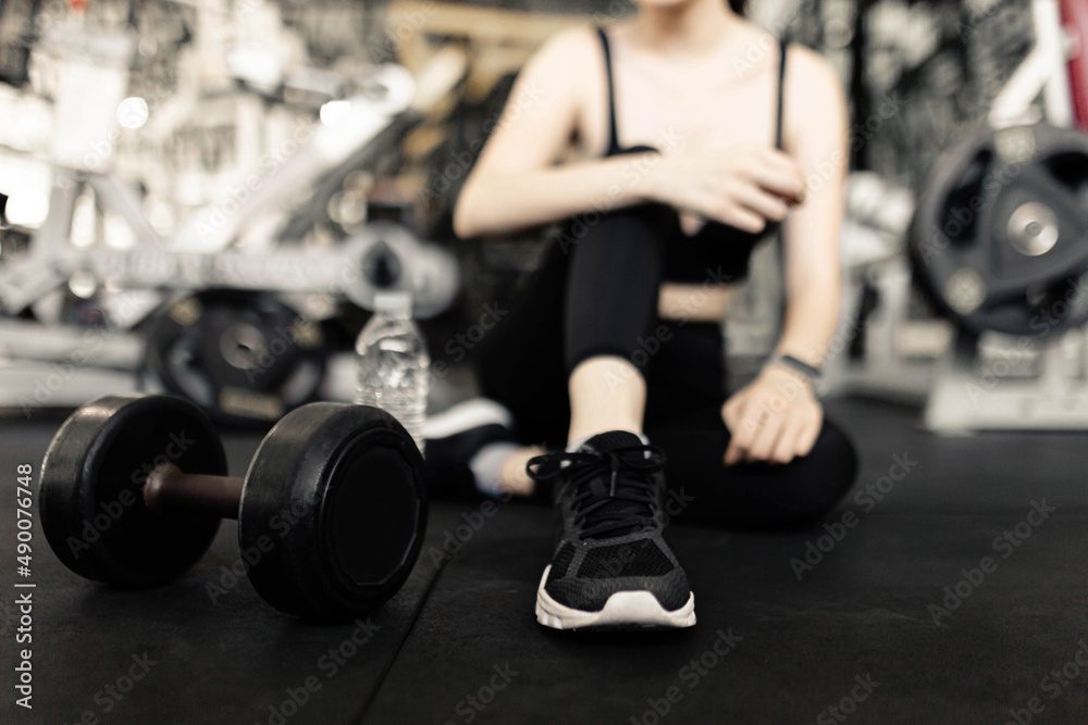 exercise concept The female with dark tone of outfits resting herself on the black carpet floor after playing on the dumbbell beside her exercise concept The female with dark tone of outfits resting herself on the black carpet floor after playing on the dumbbell beside her