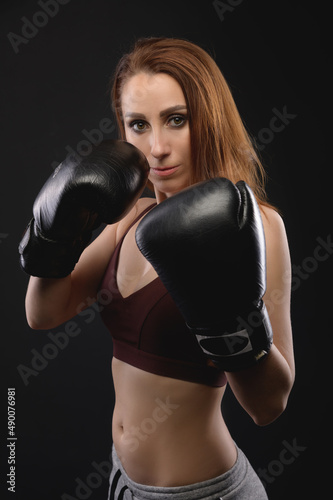 Strong and strict caucasian woman fighter in sportswear and boxing gloves on a black background. Feminism and combat sports