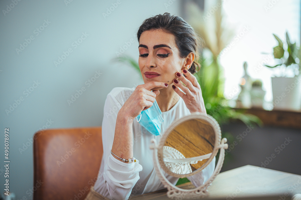 Young woman wearing medical face mask and white t shirt point finger at pimple on chin. Health care concept. Worried about acne caused by wearing a mask. Maskne. Problems with acne.