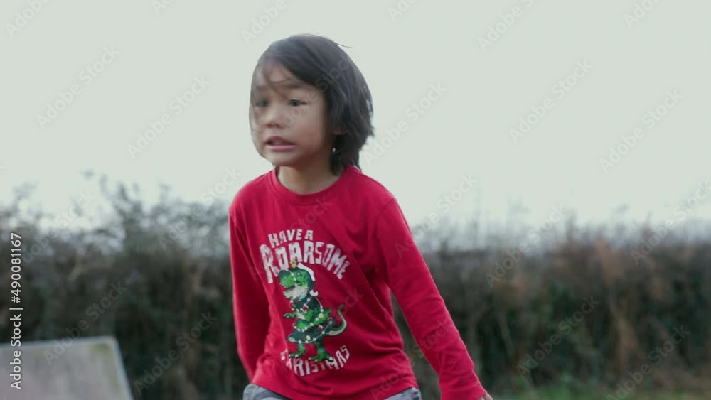 Handheld shot of Asian boy jumping up and down and brushing the hair out of his eyes.