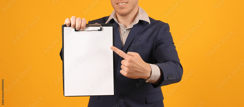 businessman in a dark suit shows a finger on a blank tablet with a clip on a yellow background, mock up