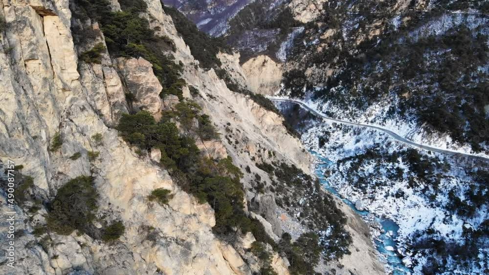Aerial view of a sheer cliff with a rare juniper with a river of clear turquoise water in the winter season high in the mountains. Sources of mountain and clean water in natural nature Aerial view of a sheer cliff with a rare juniper with a river of clear turquoise water in the winter season high in the mountains. Sources of mountain and clean water in natural nature