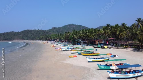 Tourists strolling along the golden sands near the coastline with moored fishing boats in Palolem Beach, in Goa, India - Aerial Fly-over
 photo