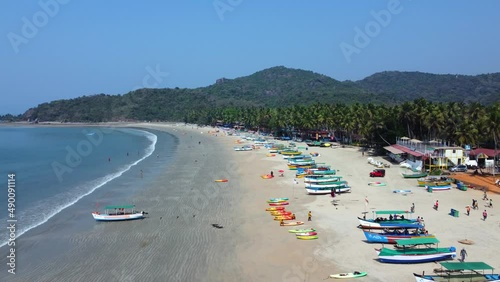 Tourists strolling along the golden sands near the coastline with moored fishing boats in Palolem Beach, in Goa, India - Aerial Fly-over
 photo