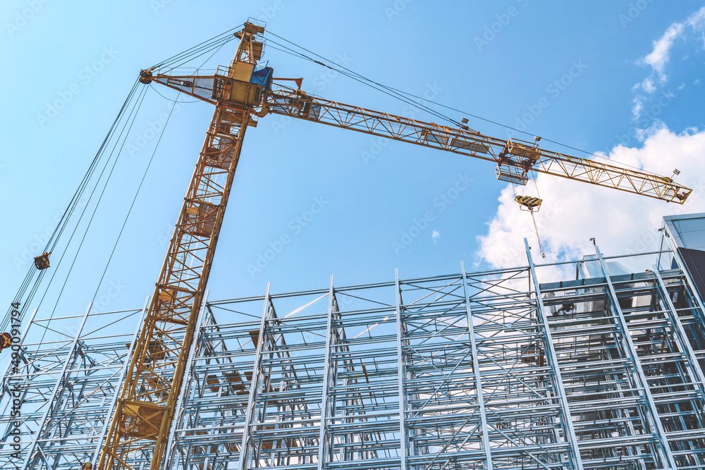 Construction crane with a new steel structure building. Against the background of a blue sky with clouds.