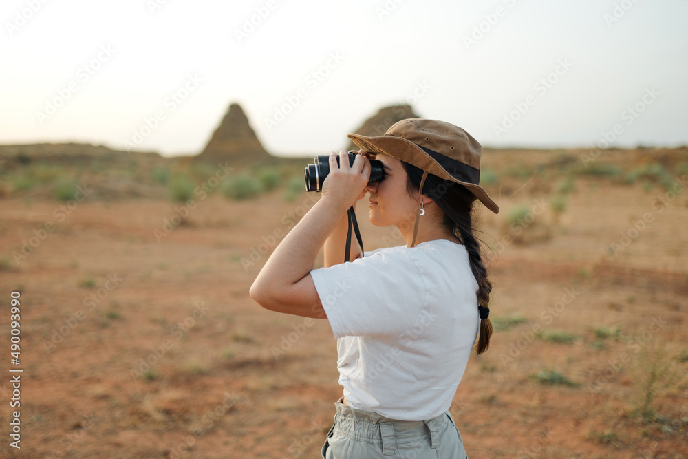 Woman looking through binoculars in desert area Woman looking through binoculars in desert area