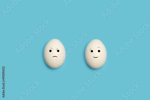 Huevos blancos con gesto sonriente feliz y enfado triste sobre un fondo celeste liso y aislado. Vista superior. Copy space