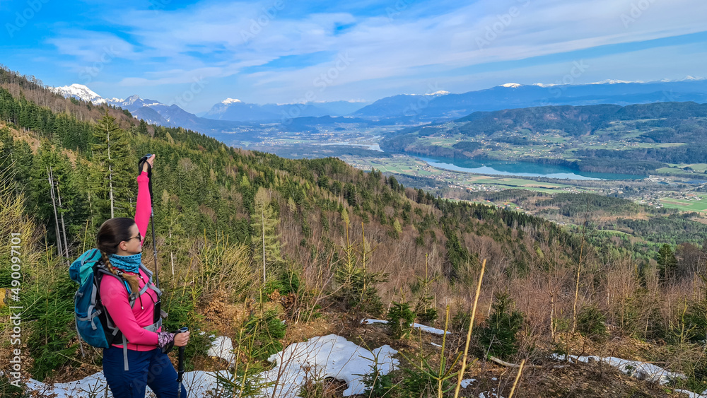 Man with backpack and a scenic view on the Drava river in the Rosental valley on the way to Sinacher Gupf in Carinthia, Austria. Forest in early spring. Austrian Alps mountain ranges on sunny day