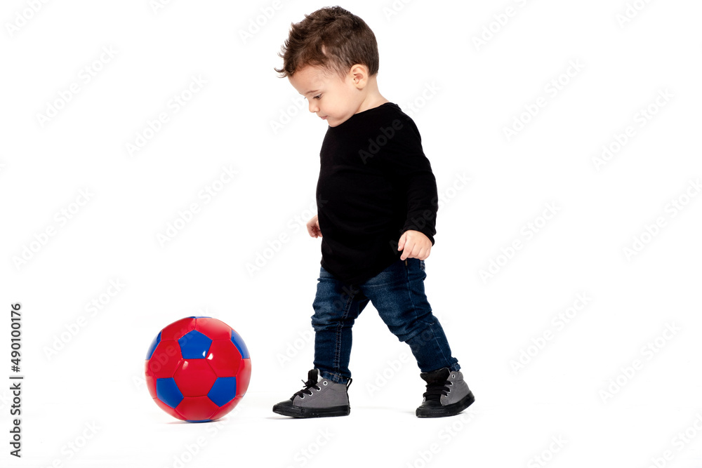  beautiful 1 year old baby boy plays with a soccer ball, white background, isolated, kicks the ball, baby chasing the soccer ball