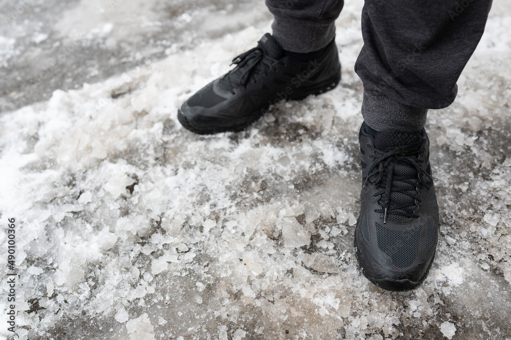 A man in winter waterproof sneakers stands on an icy road, shoes for winter walks. Walks in the open air. A man in winter waterproof sneakers stands on an icy road, shoes for winter walks. Walks in the open air.