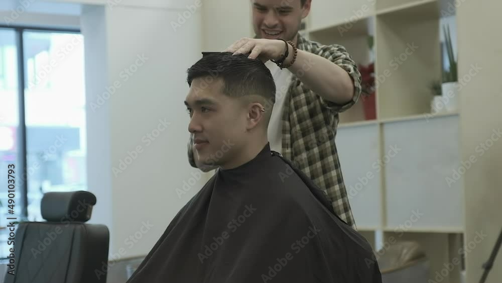 Receiving a skin fade hair cut, young Asian man is at ease with barber