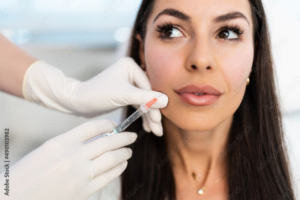Attractive woman is getting a rejuvenating facial injections at beauty clinic. The expert beautician is filling female wrinkles with botulinum toxin injections or hyaluronic acid fillers. Attractive woman is getting a rejuvenating facial injections at beauty clinic. The expert beautician is filling female wrinkles with botulinum toxin injections or hyaluronic acid fillers.