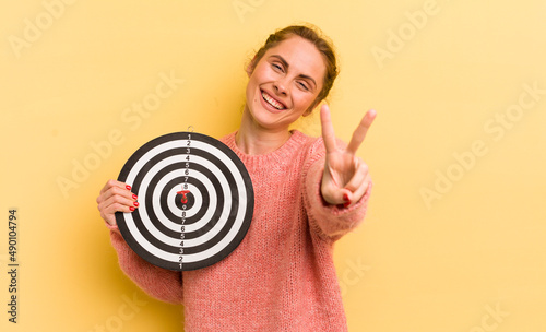 young pretty woman smiling and looking friendly, showing number two. dart target concept photo