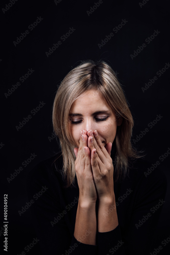 Frightened woman with hands hiding nose and mouth being silent dressed in black blouse on black background. Victim of physical and psychological abuse. Gaslighting. Relative aggression. Frightened woman with hands hiding nose and mouth being silent dressed in black blouse on black background. Victim of physical and psychological abuse. Gaslighting. Relative aggression.