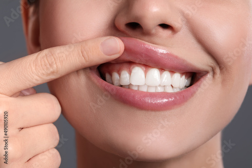 Young woman showing healthy gums on grey background, closeup photo
