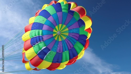 A multi-colored fluttering parachute against a blue sky with cirrus clouds. Parasailing on the sea coast.