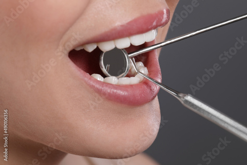 Examining woman's teeth with dentist's mirror on grey background, closeup © New Africa
