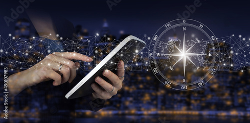 Global technologies concept. Hand touch white tablet with digital hologram compass sign on city dark blurred background. Abstract world network connection, internet and global connection concept.