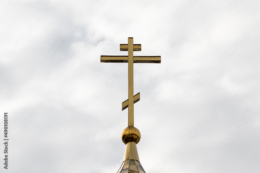 An Orthodox cross on top of the church dome against a cloudy cloudy sky.
